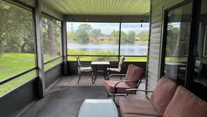 A covered porch with a table and chairs, a cushioned bench, and a view of a lake. - Lakefront 3-bedroom house in Sanford (Sanford)