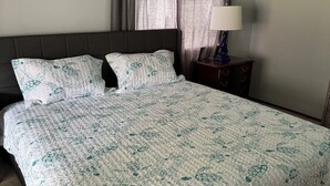 A bed with a patterned bedspread, a headboard, two pillows, a nightstand with a lamp, and a window with curtains. - Lakefront 3-bedroom house in Sanford (Sanford)