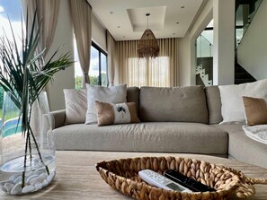 Ein modernes Wohnzimmer mit einem beigefarbenen Sofa, einer Glasvase mit Pflanzen und einem gewebten Korb für Fernbedienungen.