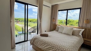 Un dormitorio moderno con una cama grande, un balcón con mesa y sillas, y vistas a zonas verdes.
