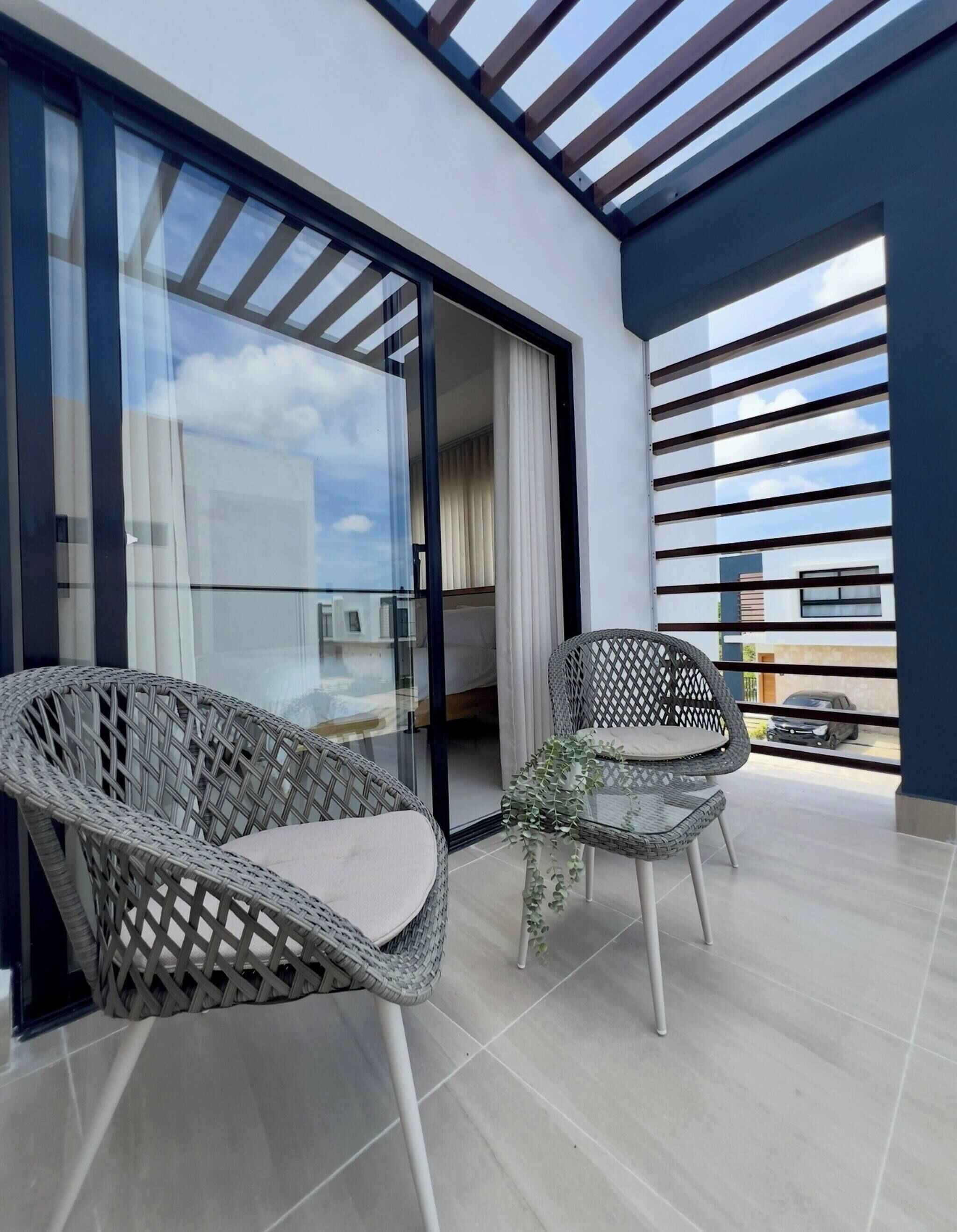 Ein Balkon mit Korbstühlen, einer Glastür und Blick auf den Himmel.