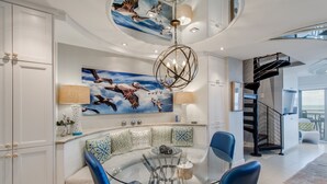 A modern interior with a curved seating area, a glass dining table, and a staircase. - Oceanfront Penthouse | 6th Floor Views + 2 King Suites (Kiawah Island)