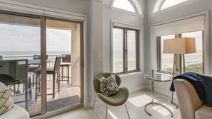 A modern room with a balcony, a chair with a decorative pillow, a round table, and a lamp. - Oceanfront Penthouse | 6th Floor Views + 2 King Suites (Kiawah Island)
