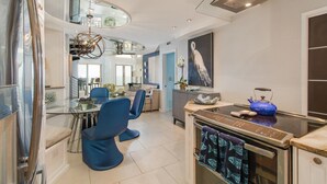A modern kitchen with a built-in oven, a blue kettle, and a dining area with blue chairs. - Oceanfront Penthouse | 6th Floor Views + 2 King Suites (Kiawah Island)