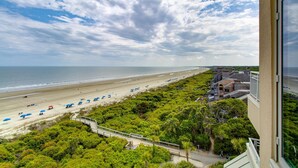 A beach view from a window overlooking a sandy beach with umbrellas, a pathway, and lush greenery. - Oceanfront Penthouse | 6th Floor Views + 2 King Suites (Kiawah Island)