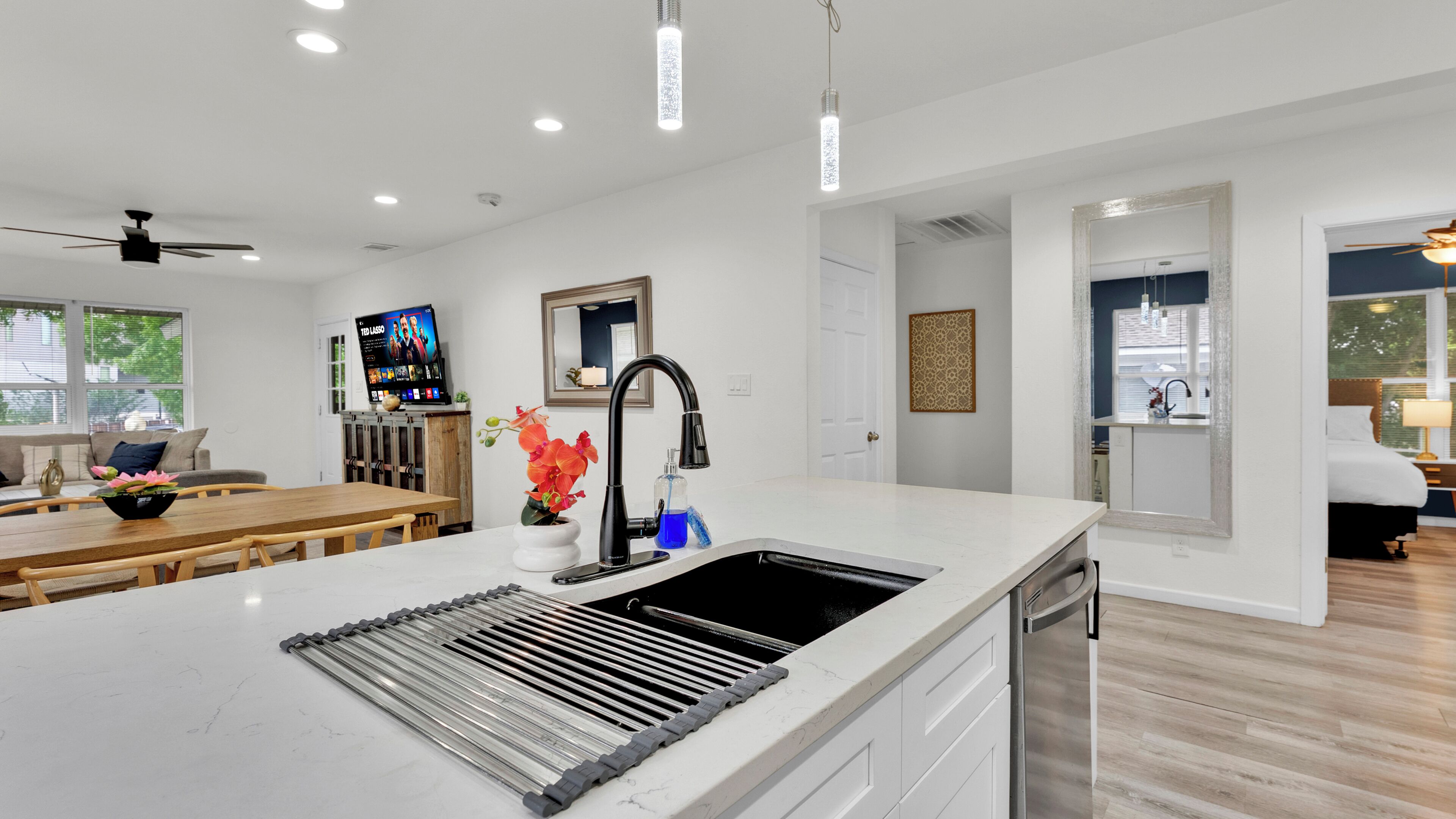 A modern kitchen with a large island, a dining area with a wooden table, and a living room with a sofa.