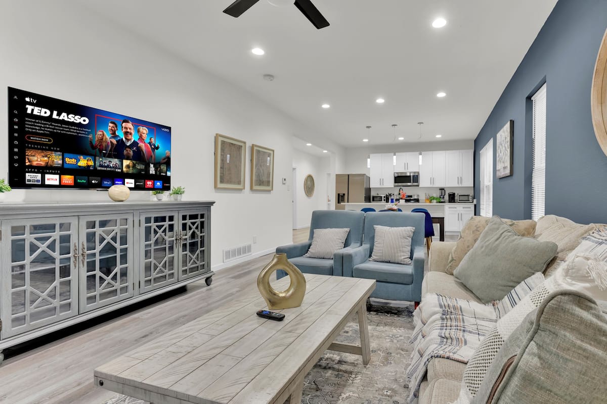 A modern living room with a flat-screen TV, a grey cabinet, a blue sofa, and a patterned rug.