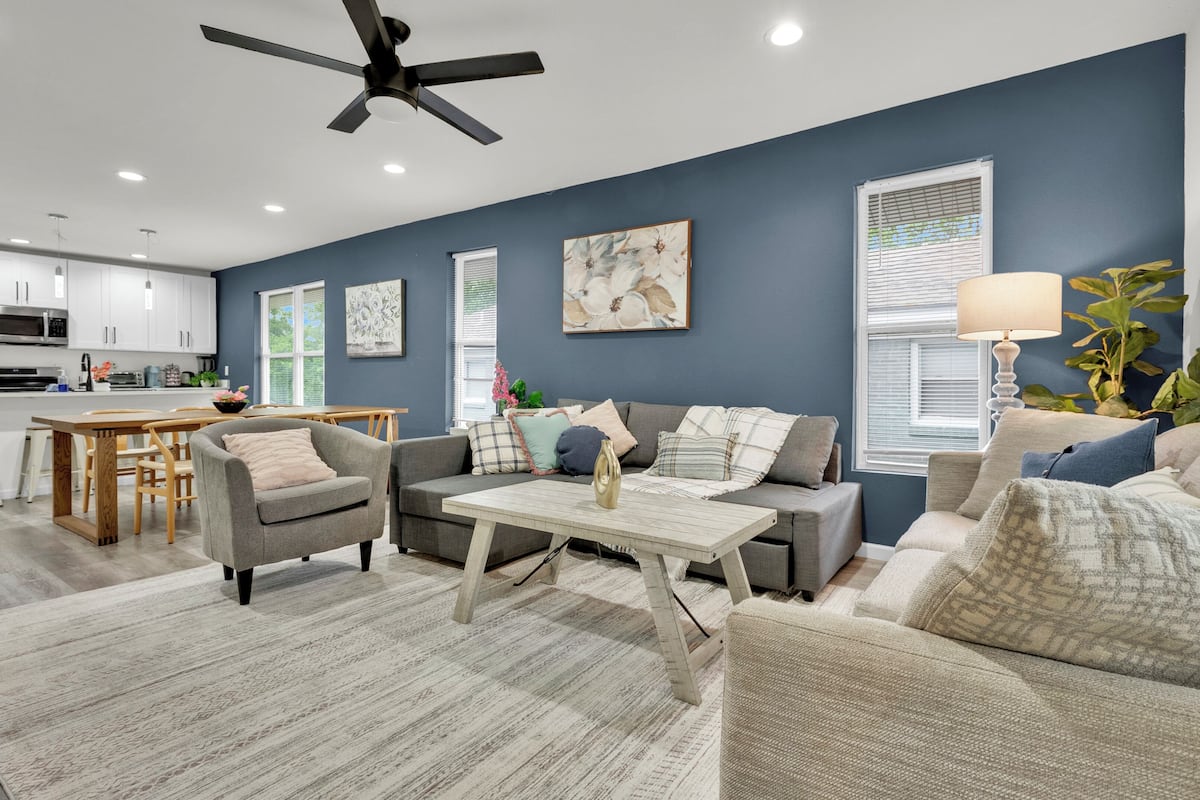 A modern living room with a sofa, armchairs, and a coffee table. There is a kitchen area with cabinets and a microwave.