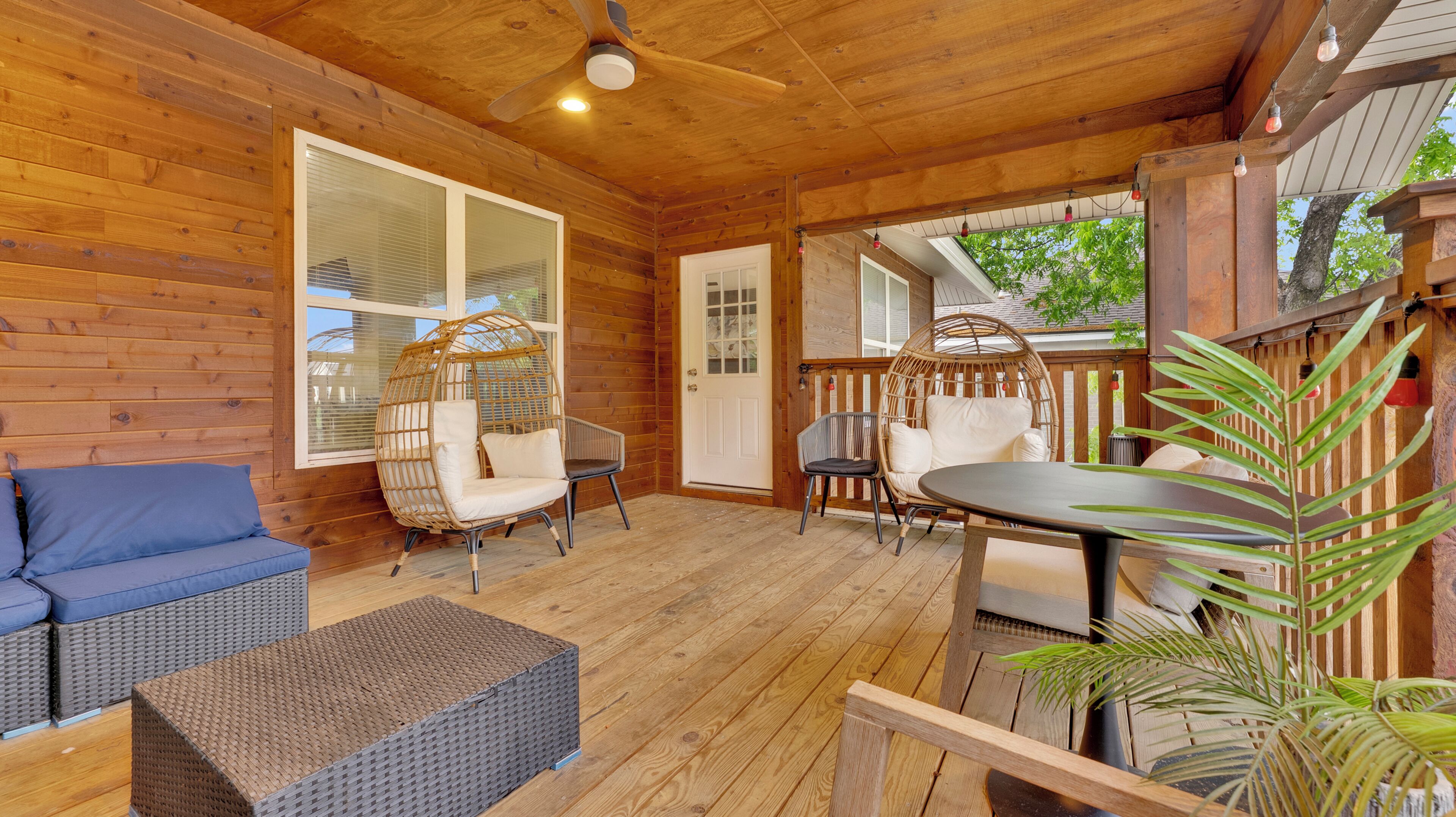 Eine Holzterrasse mit Korbmöbeln, einem Deckenventilator und Blick ins Freie.