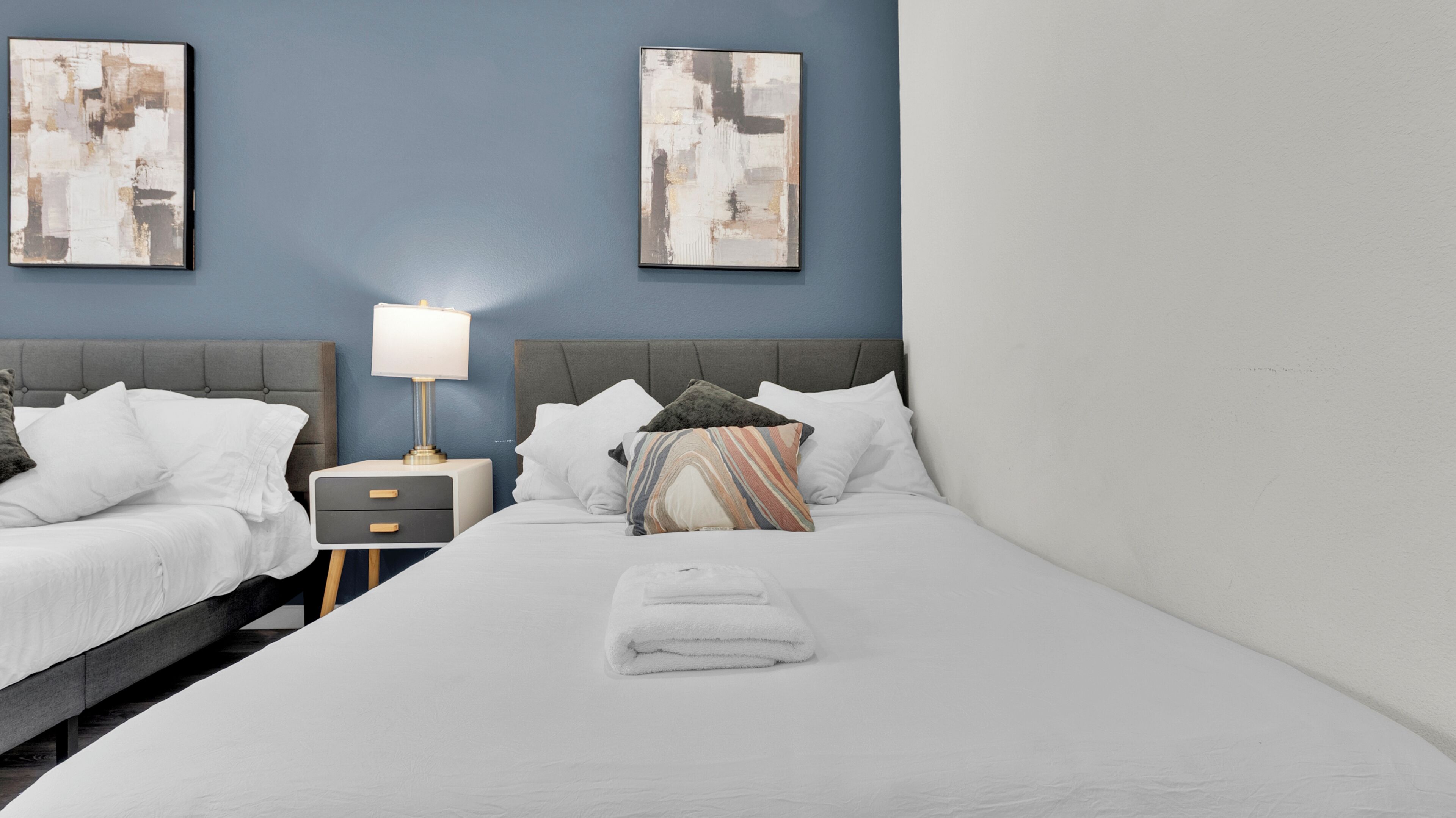 Una habitación de hotel con una cama, dos mesitas de noche, una lámpara y obras de arte abstracto en las paredes.