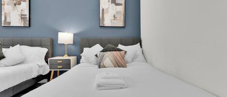 Una habitación de hotel con una cama, dos mesitas de noche, una lámpara y obras de arte abstracto en las paredes.