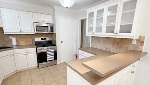 A kitchen with white cabinets, a stainless steel stove, a microwave, and a tiled floor.