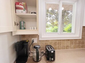 Una cocina con ventana, cafetera, tostadora y un armario con diversos objetos.