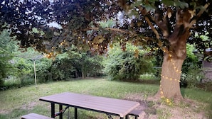 Ett picknickbord med bänkar på en gräsig utomhusplats med träd och ljusslingor.