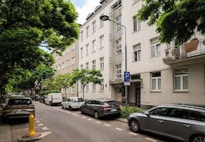 Een straat met geparkeerde auto's, een gele paal en een gebouw met een blauw parkeersignaal.