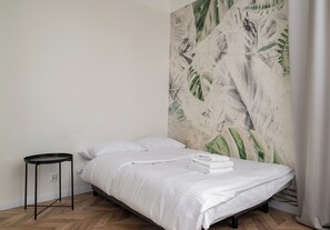 Ein Schlafzimmer mit einem Bett, weißer Bettwäsche, einem schwarzen Nachttisch und einer Wand mit Blättermotiv.