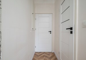 Ein Korridor mit einer weißen Tür, einem Holzboden mit Fischgrätmuster und einer weißen Wand mit Lichtschalter.