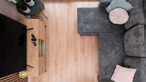 A modern living room with a sectional sofa, a flat-screen TV, wooden flooring, and a skylight. - Łódź Downtown Charm Apartment (Łódź)