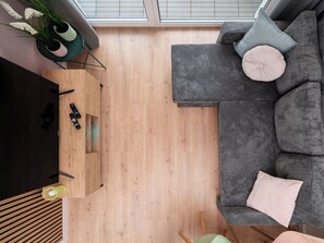 Ein modernes Wohnzimmer mit einem Ecksofa, einem Flachbildfernseher, Holzböden und einem Oberlicht.