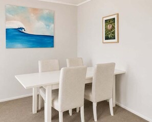 Ein Essbereich mit einem weißen Tisch, vier Stühlen, einem Wellenbild und einem gerahmten Foto an der Wand.