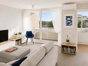 A modern living room with a sofa, a TV, a bookshelf, and a balcony with a view. - NB102 - Cremorne Comfort | Leafy 2-Bed With Harbour Glimpses (Cremorne)