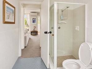 Ein Badezimmer mit einer gläsernen Duschkabine, einer weißen Toilette und einem sichtbaren Duschbereich.