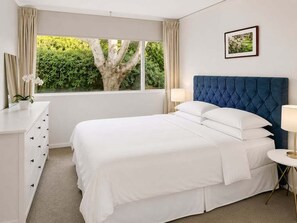 A bedroom with a bed, a dresser, a bedside table, a lamp, a window with a view of greenery, and a framed picture on the wall. - NB102 - Cremorne Comfort | Leafy 2-Bed With Harbour Glimpses (Cremorne)