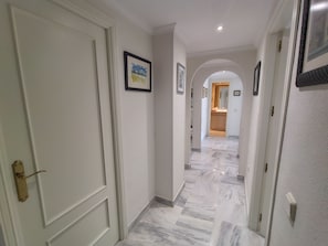 A hallway with marble flooring, white walls, and framed pictures. - Relax in Banus - 3 bedrooms, pools, paddle - Pass the Keys (Marbella)