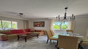 En stue med sofasæt, spisebord med stole, en lysekrone og et maleri på væggen.