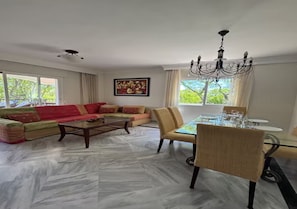 A living room with a sofa set, a dining table with chairs, a chandelier, and a painting on the wall. - Relax in Banus - 3 bedrooms, pools, paddle - Pass the Keys (Marbella)