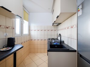 Une cuisine de taille réduite, équipée d’une cuisinière à gaz, d’un évier et d’une fenêtre.