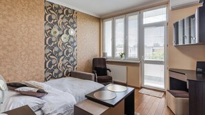 Ein modernes Hotelzimmer mit Bett, Nachttisch, Sessel, Schreibtisch und großen Fenstern mit Jalousien.