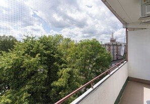 Ein Balkon mit Blick auf Bäume und Gebäude, einem Geländer und einem klaren Himmel.
