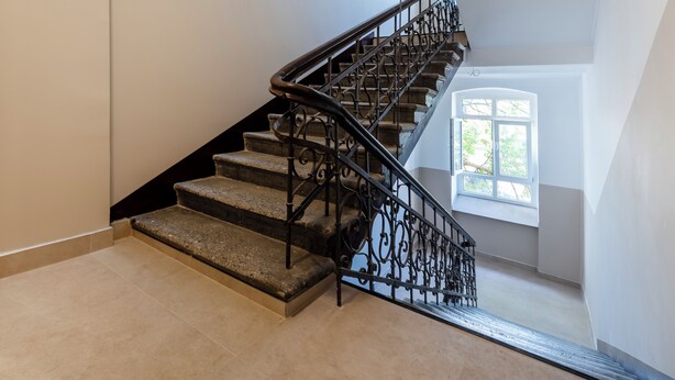 A staircase with a wrought iron railing, a window with a view of greenery, and a light-colored floor. - Skierniewicka Charm Studio (Łódź)
