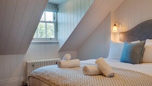 Una camera da letto con soffitto spiovente, un letto con asciugamani arrotolati, una finestra vista e un lampadario a parete.