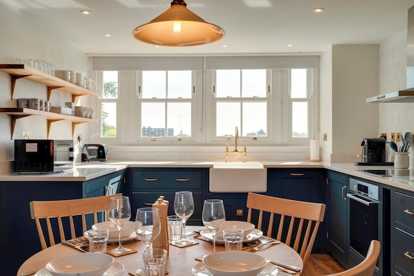 A modern kitchen with a dining area, featuring a large window, dark blue cabinets, and a central island. - Luxury stay in the Cambridge City Centre - Flat 5 - Pass the Keys (Cambridge)