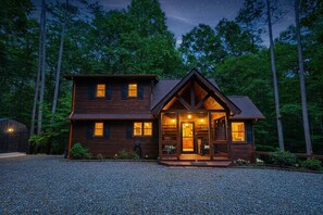 Eine zweistöckige Holzhütte mit Veranda, umgeben von einem Wald.