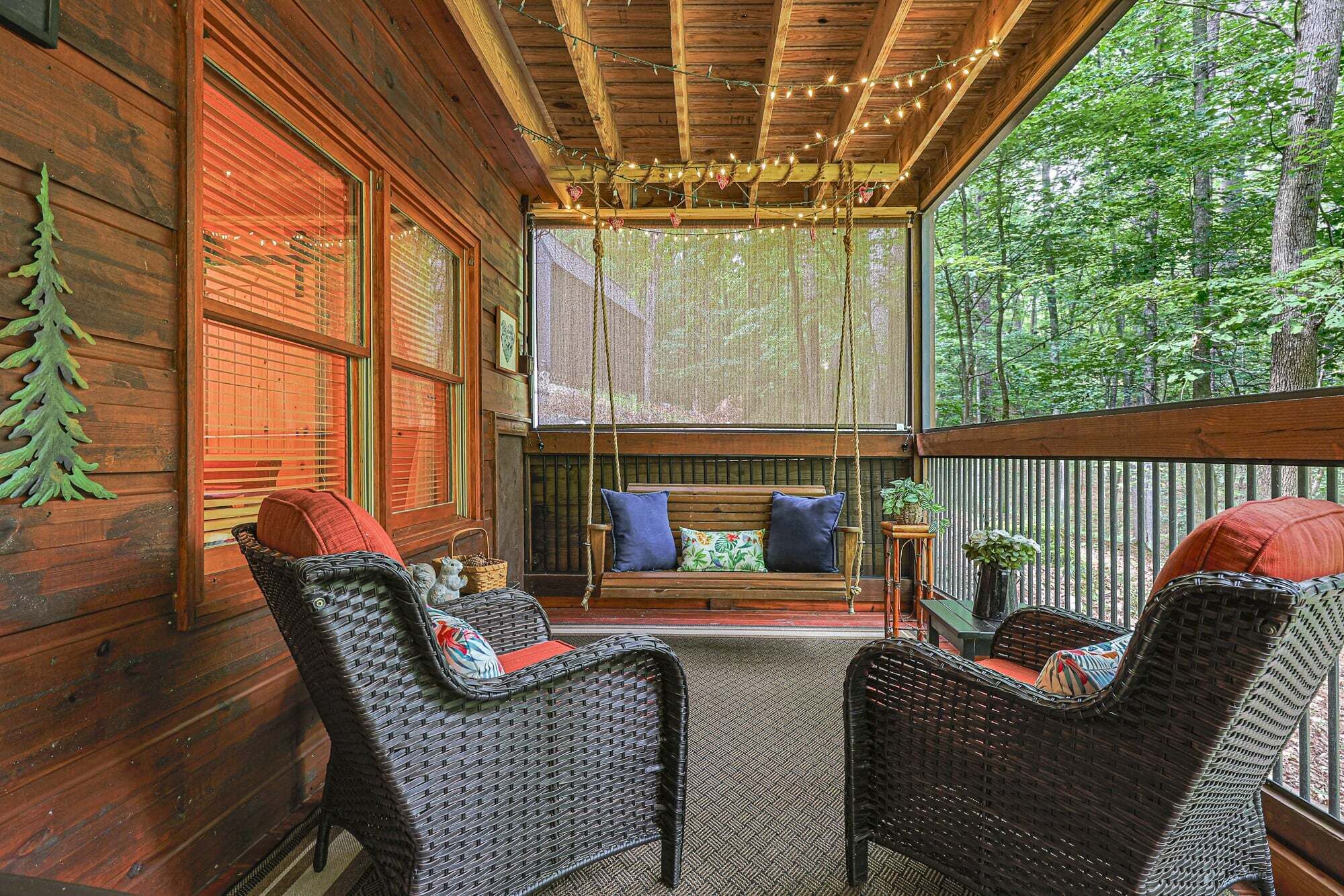 A wooden porch with wicker chairs, a swing, and a view of the forest.
