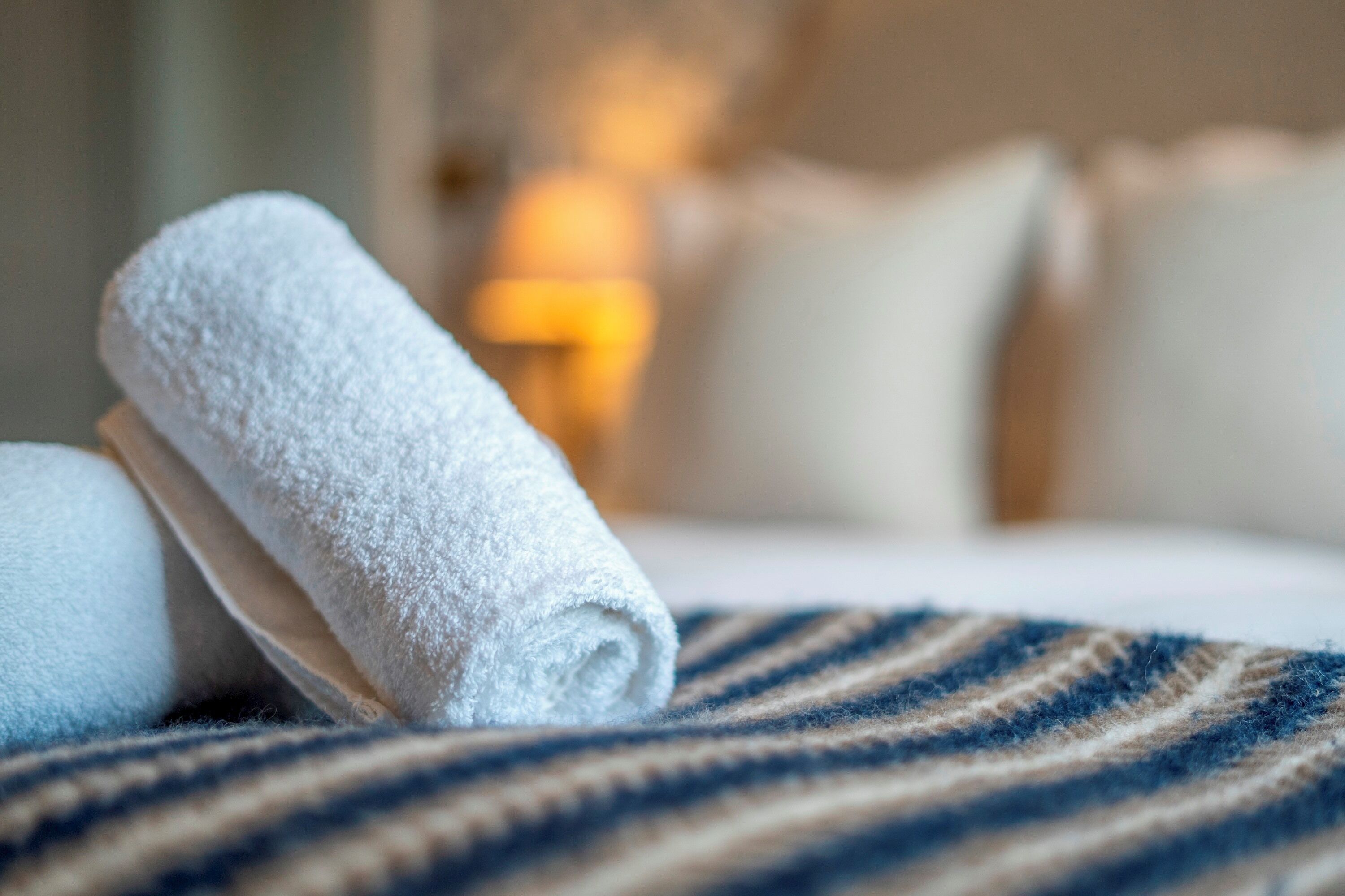 A neatly made bed with a striped blanket and rolled white towels.