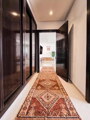 Un pasillo con alfombra estampada, puertas de madera oscura y vista a una habitación con televisor y muebles.