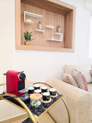 Una sala de estar moderna con una cafetera roja, una mesa de mármol y un sofá color beige.