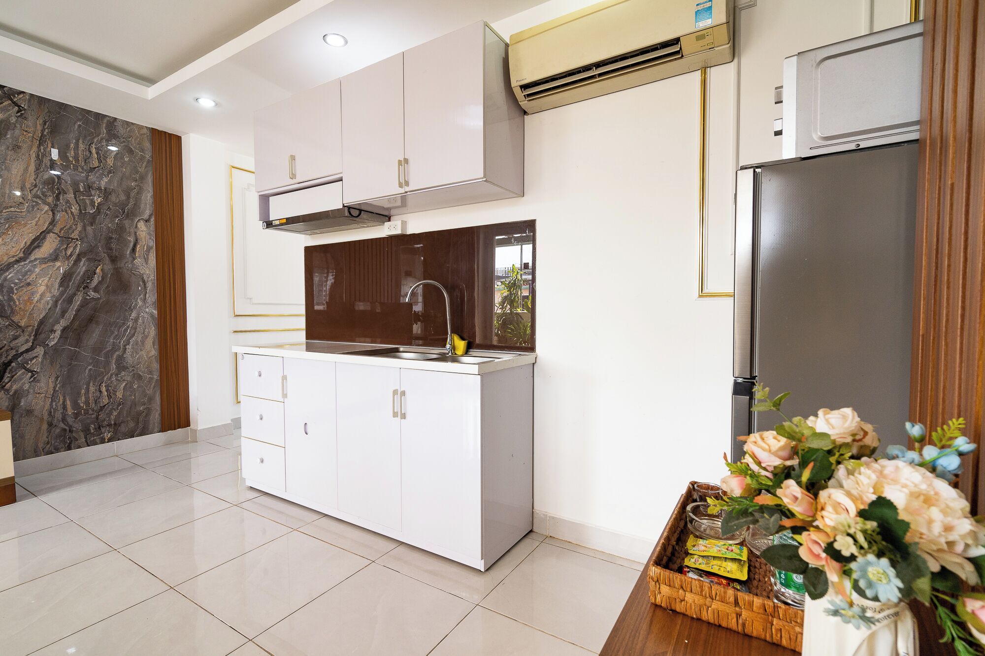 Una cocina moderna con armarios blancos, un lavamanos de acero inoxidable y un equipo de aire acondicionado.