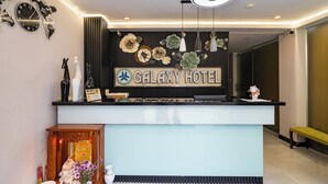 Ein Hotelrezeptionstresen mit einem Schild, das 'Galaxy Hotel' zeigt, einer Weltkarte als Uhr und einer dekorativen Blumenkomposition.