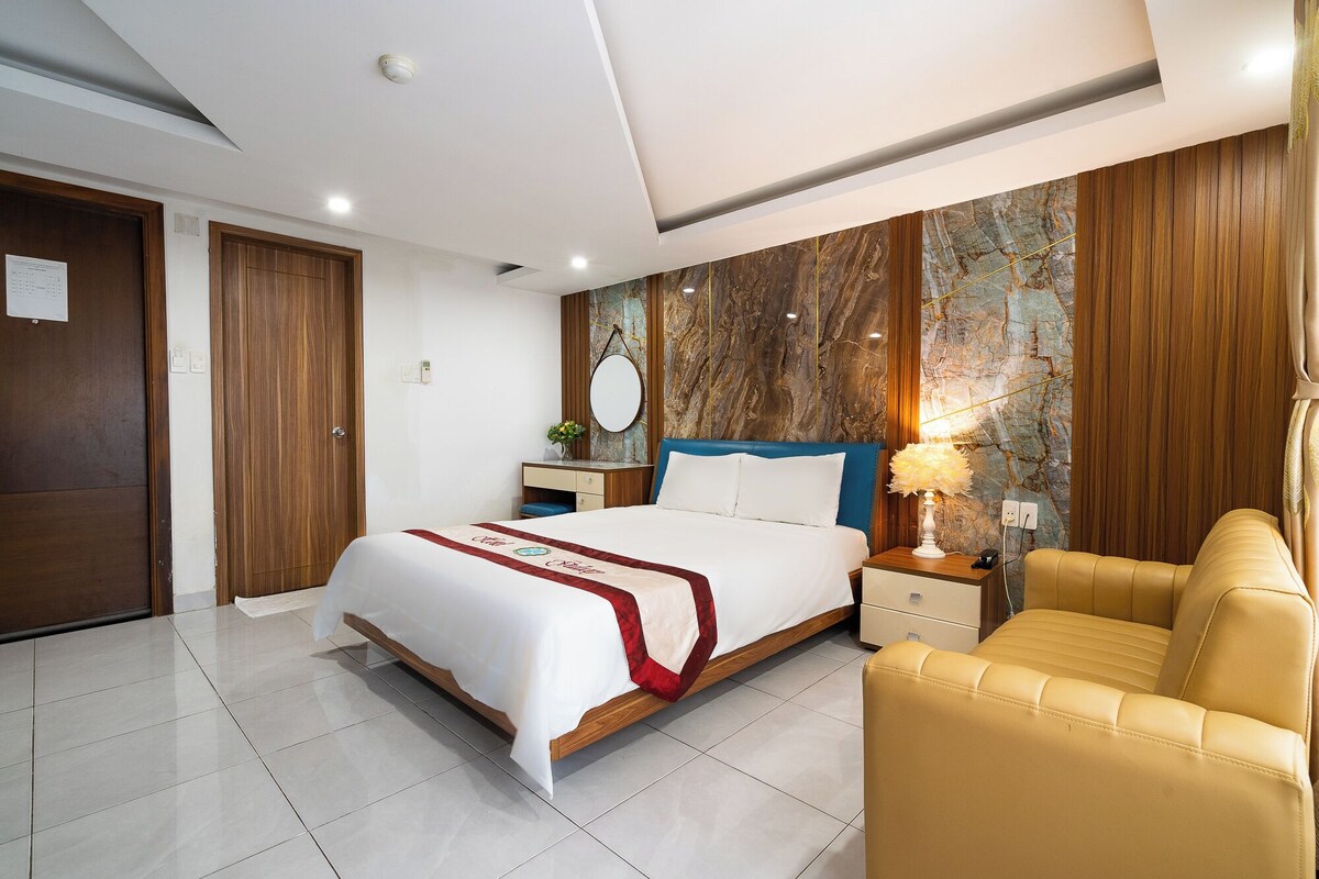 A modern hotel room with a bed, a nightstand, a lamp, a chair, and a marble wall.