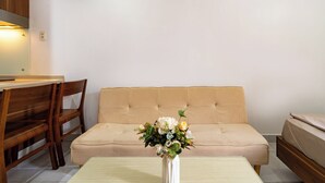 Ein Zimmer mit einer Couch, einem Holzstuhl, einem kleinen Tisch und einer Vase mit Blumen.