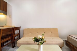 A room with a sofa, a wooden chair, a small table, and a vase with flowers. - Galaxy Hotel & Apartment Near SECC (Ho Chi Minh City)