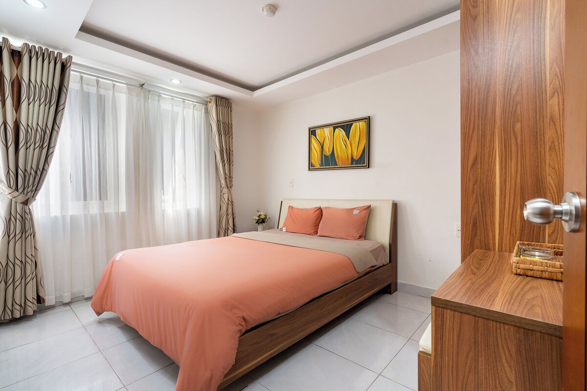 A bedroom with a bed, curtains, a painting, and a wooden cabinet.