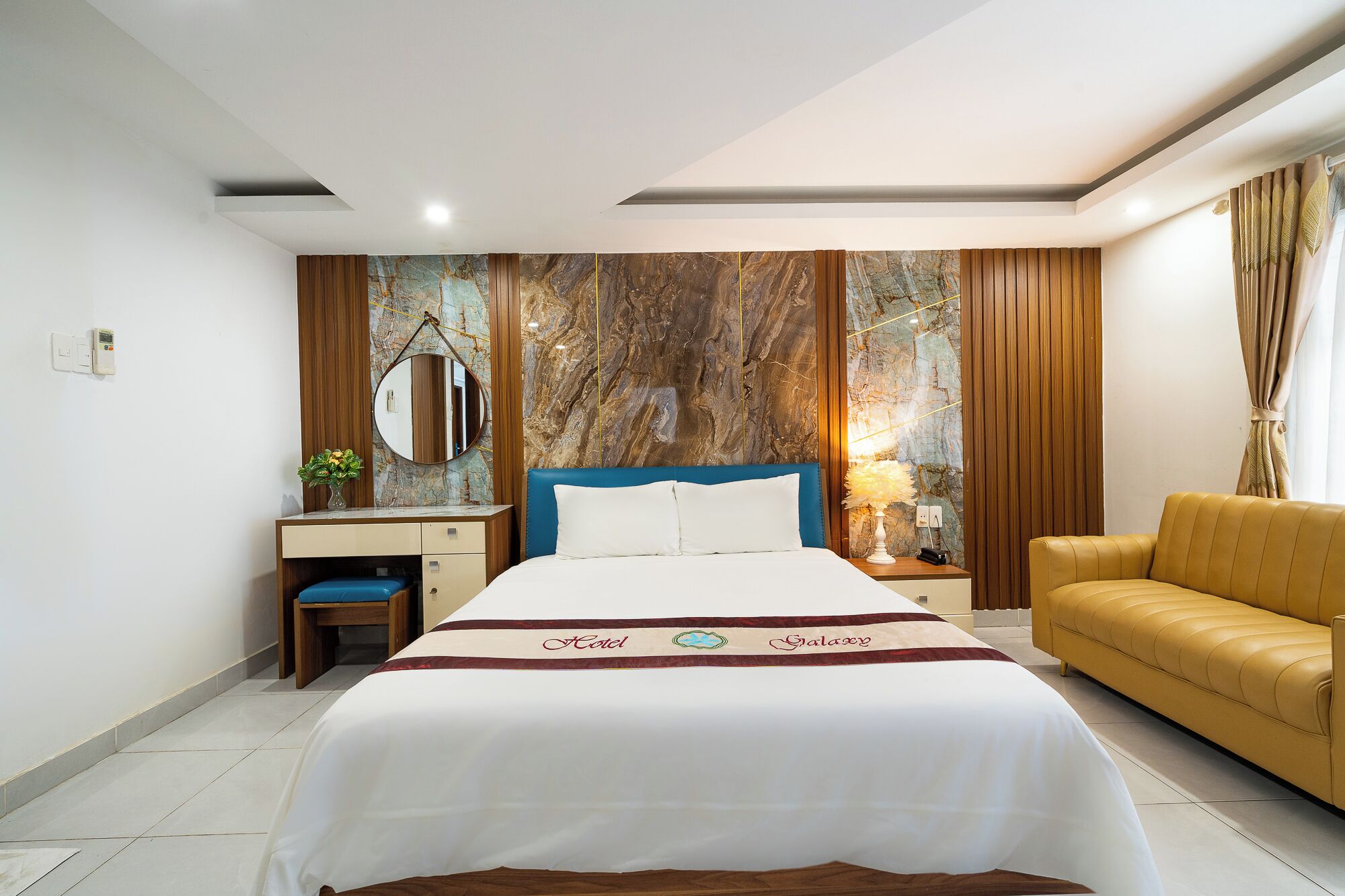 A hotel room with a bed, a desk, a chair, and a sofa.