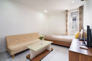 A small, modern room with a sofa, a glass-top table, a bed, a desk with a computer, and a window with curtains. - Galaxy Hotel & Apartment Near SECC (Tan Hung)