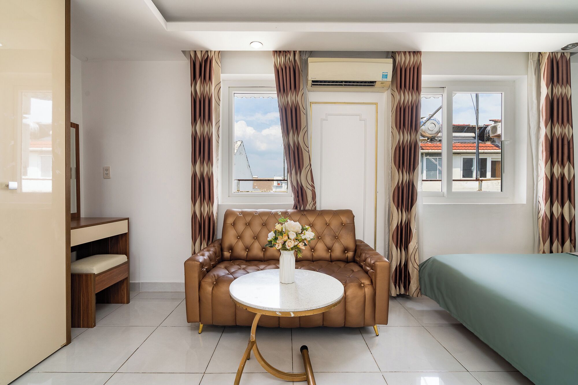 Una sala moderna con un sofá de cuero marrón, una mesa de centro redonda y una cama con cubrecama verde.